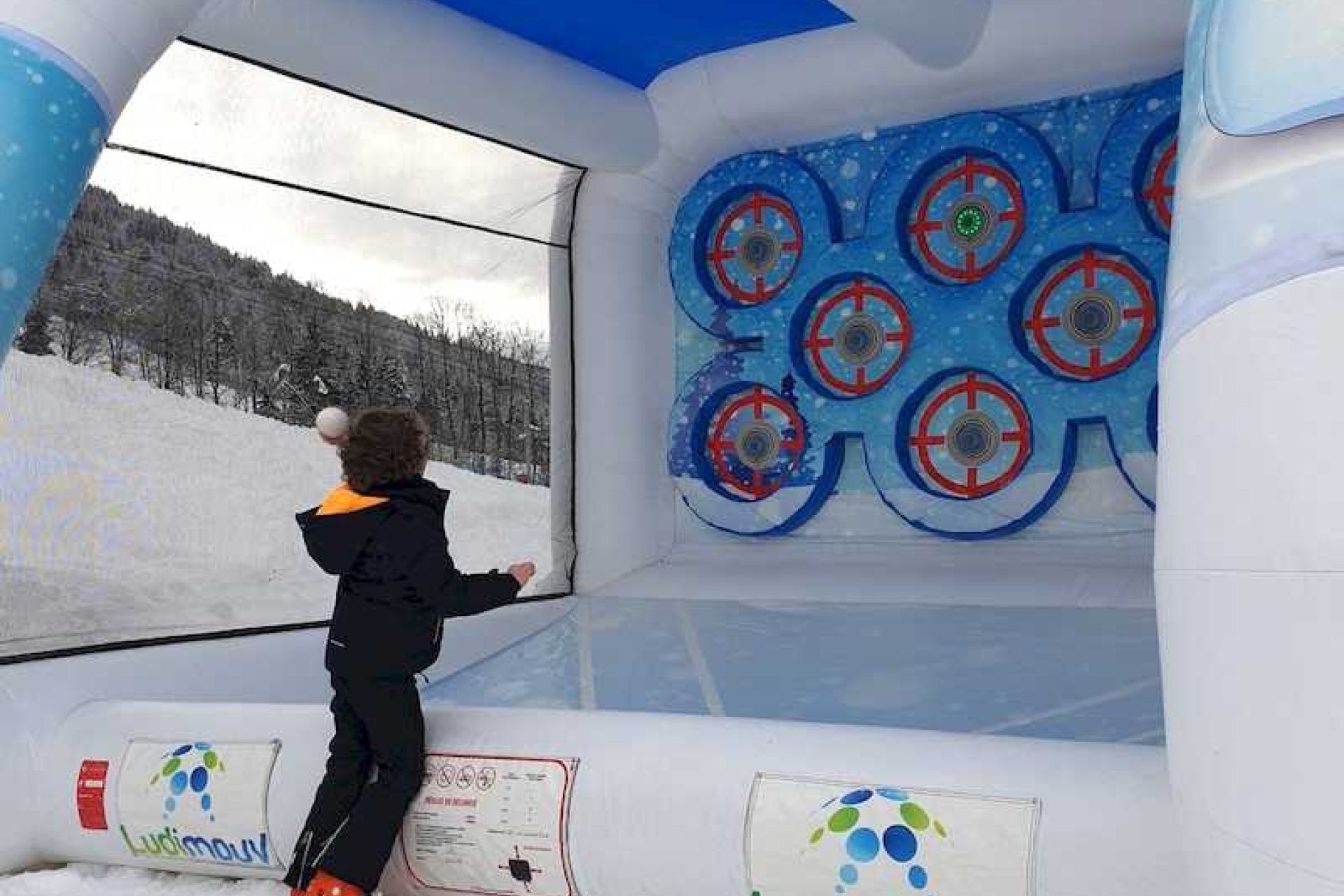 Enfant lançant une boule de neige sur une cible de la cage gonflable, installée en extérieur sur la neige.