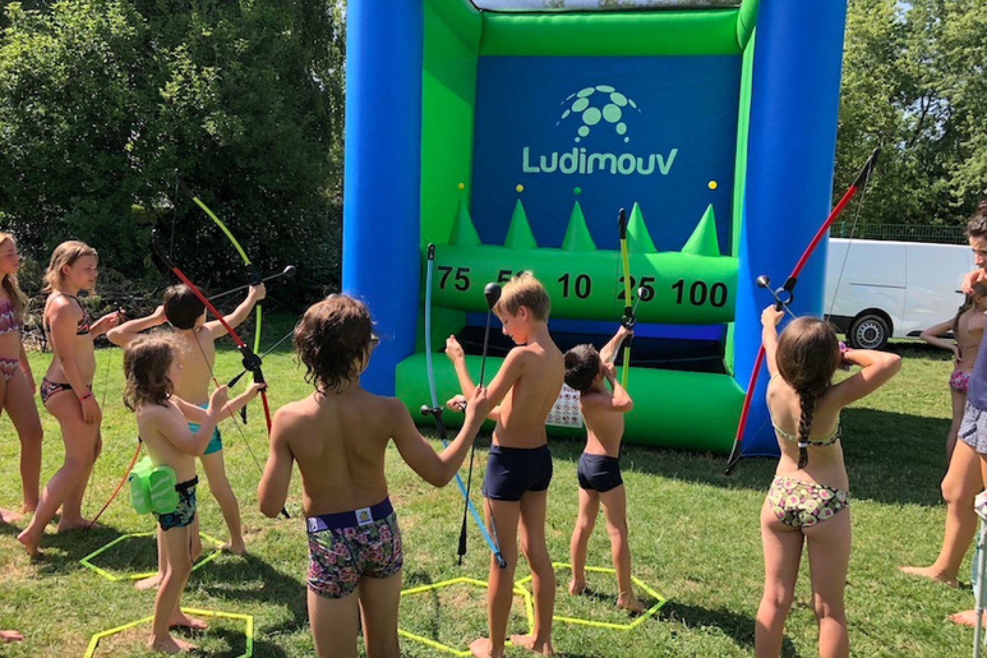 Stand de tir à l'arc gonflable en plein air pour une animation estivale, avec groupe d'enfants tirant à l'arc
