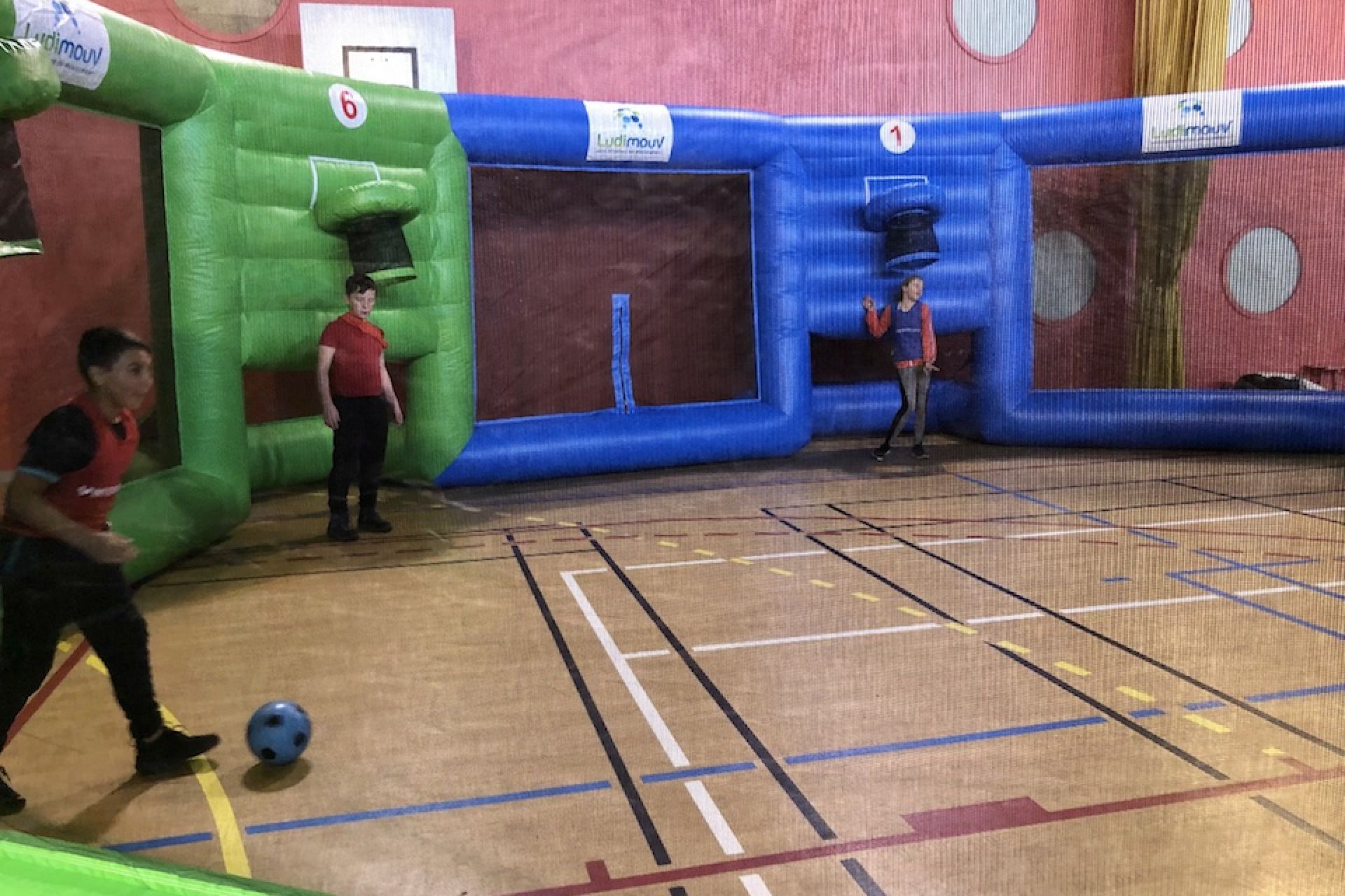 Équipes d'enfants s'affrontant au basket dans l'arène gonflable installée dans un gymnase.
