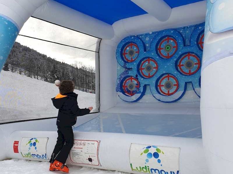 Enfant lançant une boule de neige sur une cible de la cage gonflable, installée en extérieur sur la neige.