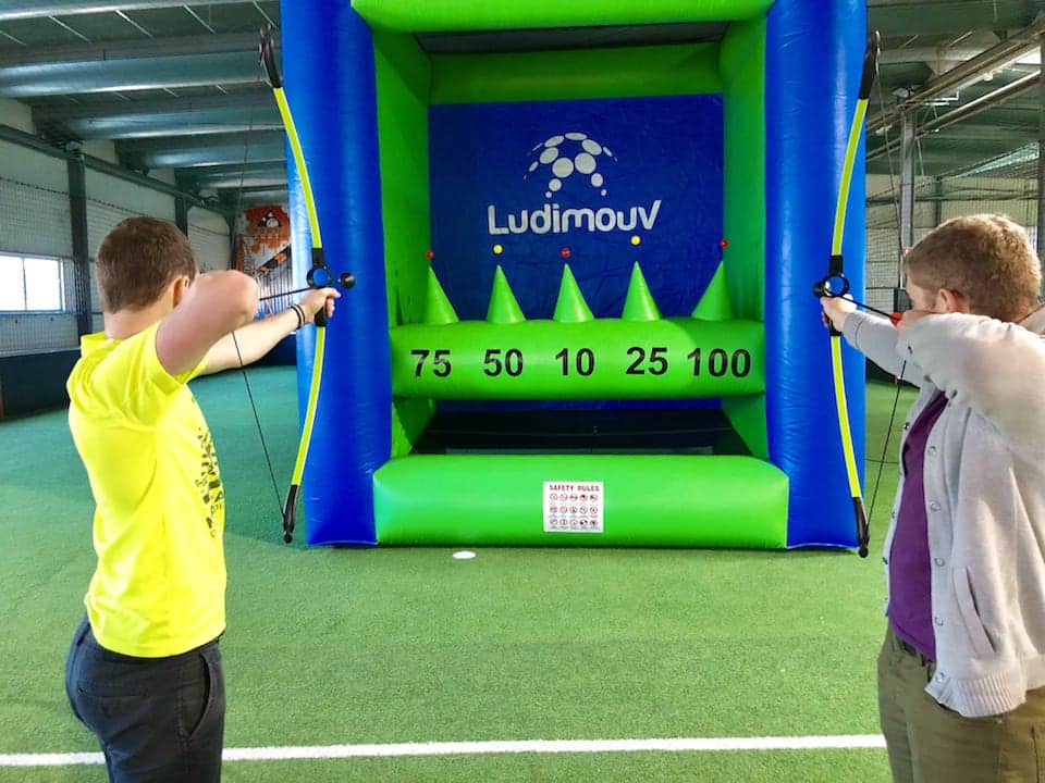 Stand de tir à l'arc gonflable installé en intérieur avec archers visant les balles en lévitation.